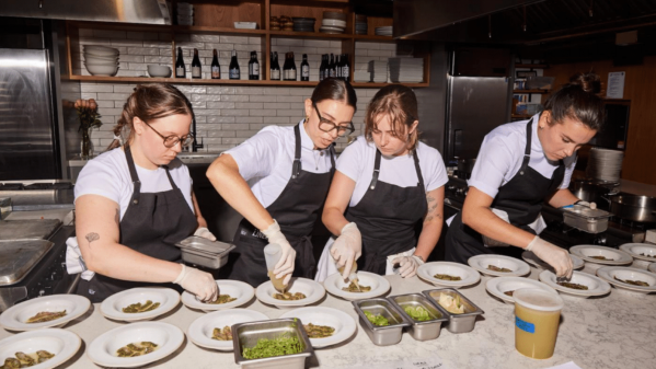 Four cooks plating dishes together along a long marble pass